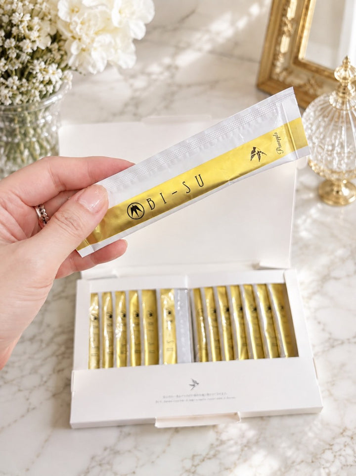 A hand lifting a BI-SU jelly stick from its box, on marble with white flowers